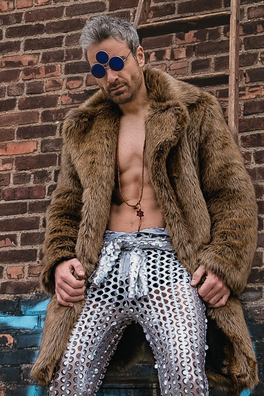 Bold festival wear from HARMONIA NY: faux fur coat, metallic chainmail pants, and tri-lens sunglasses against brick wall