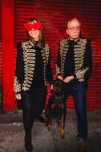 Bold festival wear from HARMONIA NY: couple in gold-embroidered jackets with dog, red backdrop