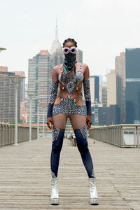 Bold festival wear by HARMONIA NY: sparkling bodysuit, mesh mask, silver boots on city pier